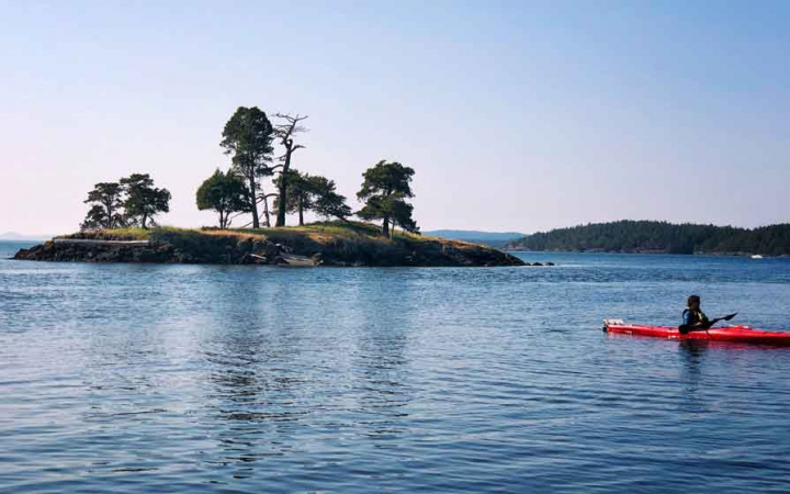 a person in a red kayak moves past an island on a kayaking trip with outward bound